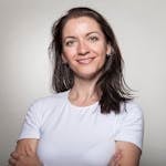 Portrait of a confident woman smiling with arms crossed, wearing a white t-shirt on a gray background.
